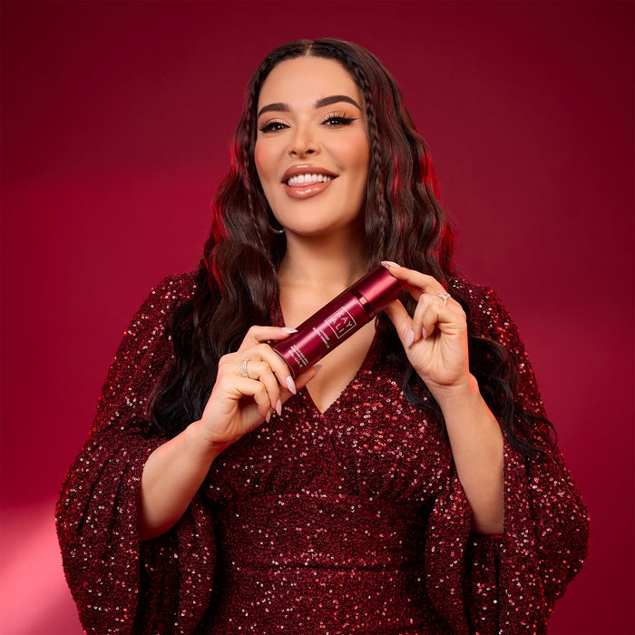 Mona Kattan in a red dress holding a red  product against a red background