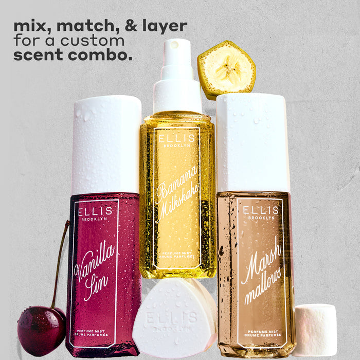 VANILLA SIN Perfume Mist 240ml next to a cherry, BANANA Milkshake Perfume Mist 240ml sitting on top of it's cap, MARSHMALLOWS Perfume Mist 240ml with a slice on banana on top of it and a marshmallow next to it, all covered in water droplets on a gray, rough background with black text that reads "mix, match, and layer for a custom scent combo."