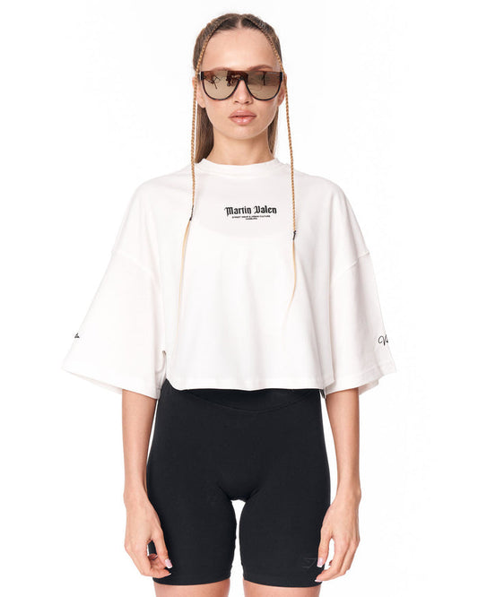A model wearing a white Martin Jakeo cropped t-shirt with wide three-quarter sleeves and black bike shorts, set against a plain white background.