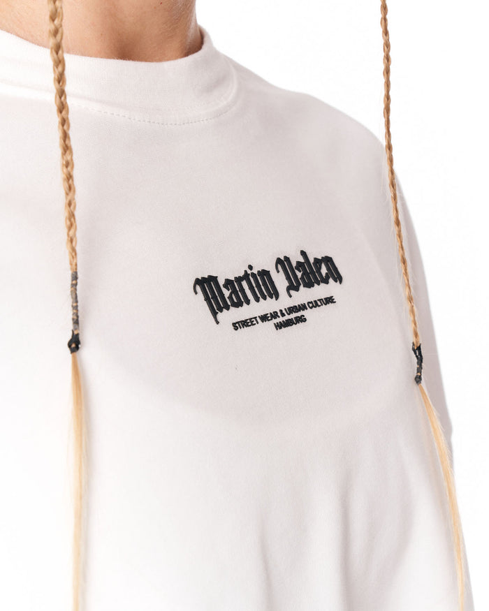 A close-up of a person wearing a white mock-neck sweatshirt with black gothic text reading 'Martin Valen' and smaller text below, against a plain white background.