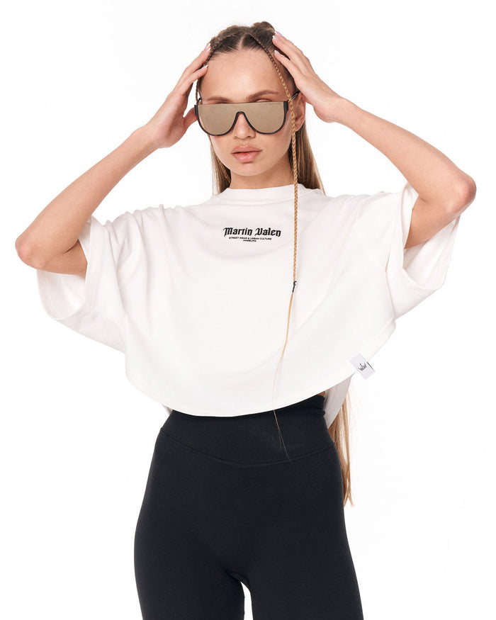A model wearing a white cropped t-shirt with 'Martin Valen' printed on the chest, paired with black leggings and sunglasses, against a plain white background.
