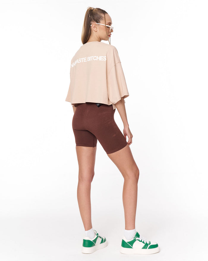 A model wearing a light beige crop top and dark brown fitted biker shorts against a plain white background.