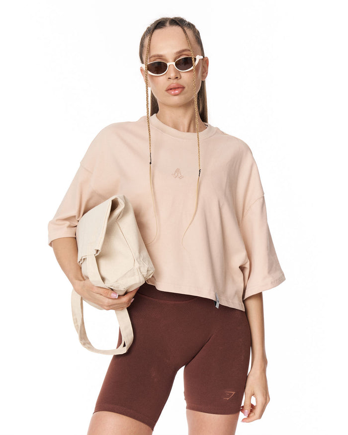 A woman modeling a light beige crop top and dark brown bike shorts against a plain white studio background.