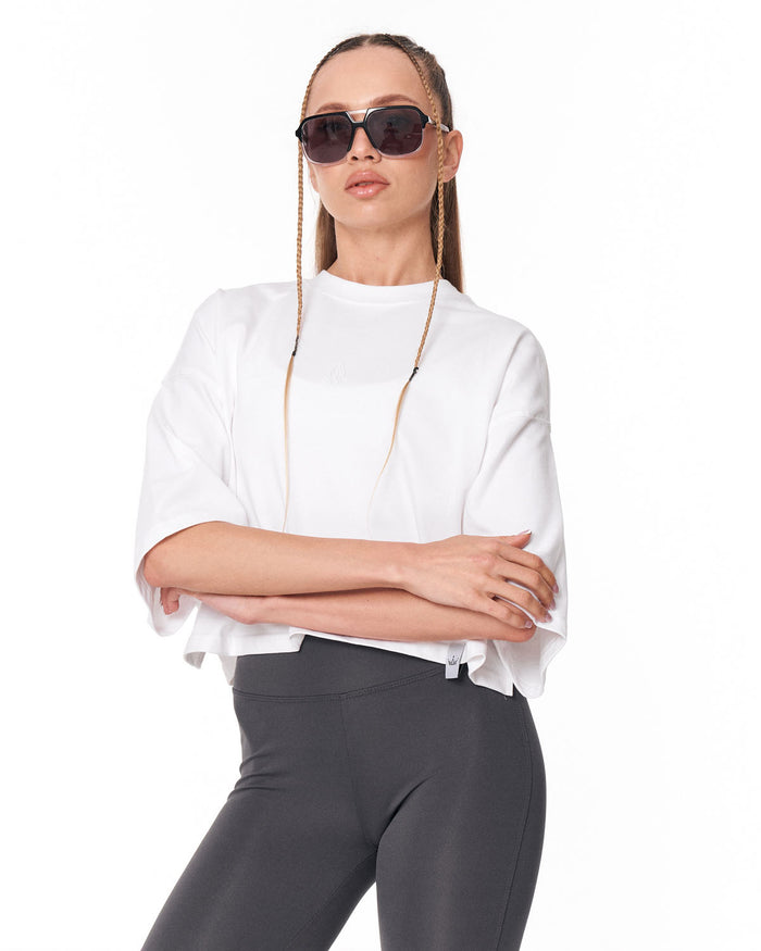 A woman modeling a white short-sleeve top and dark gray leggings against a plain white background.