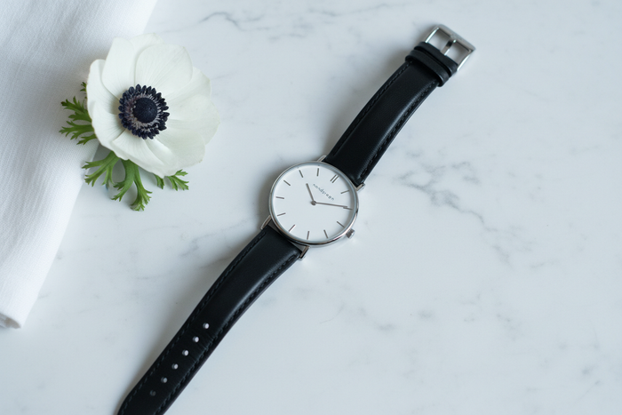 Nordgreen Native 32mm Silver Case Black Leather watch flat lay on white marble with white anemone