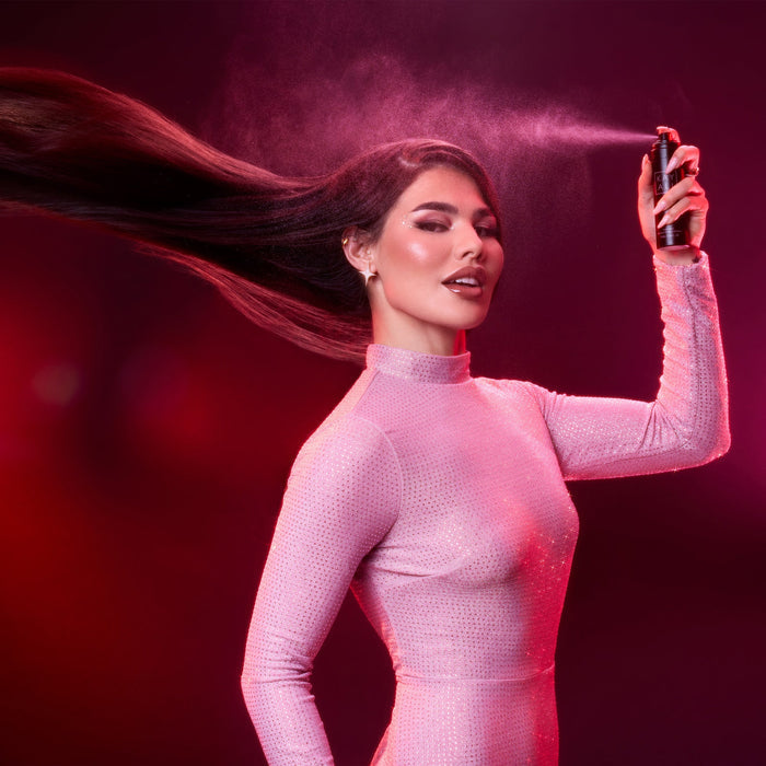 Woman in a pink outfit spraying a product against a dark background