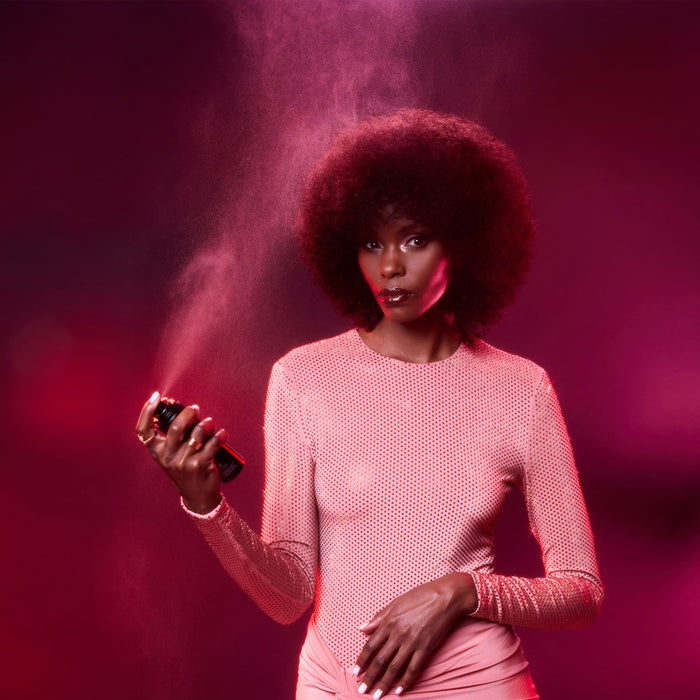 Woman holding a spray can with pink powder against a pink background