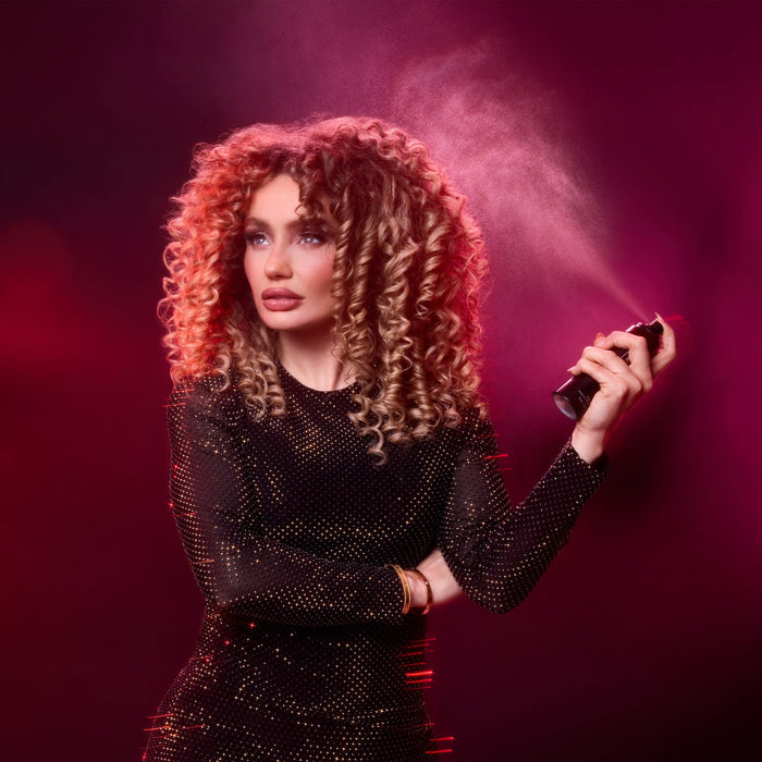 Woman with curly hair holding a makeup brush against a pink background