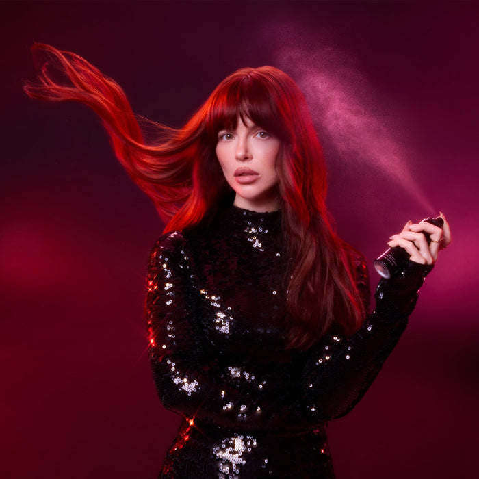 Woman with red hair holding a hair spray can against a dark background