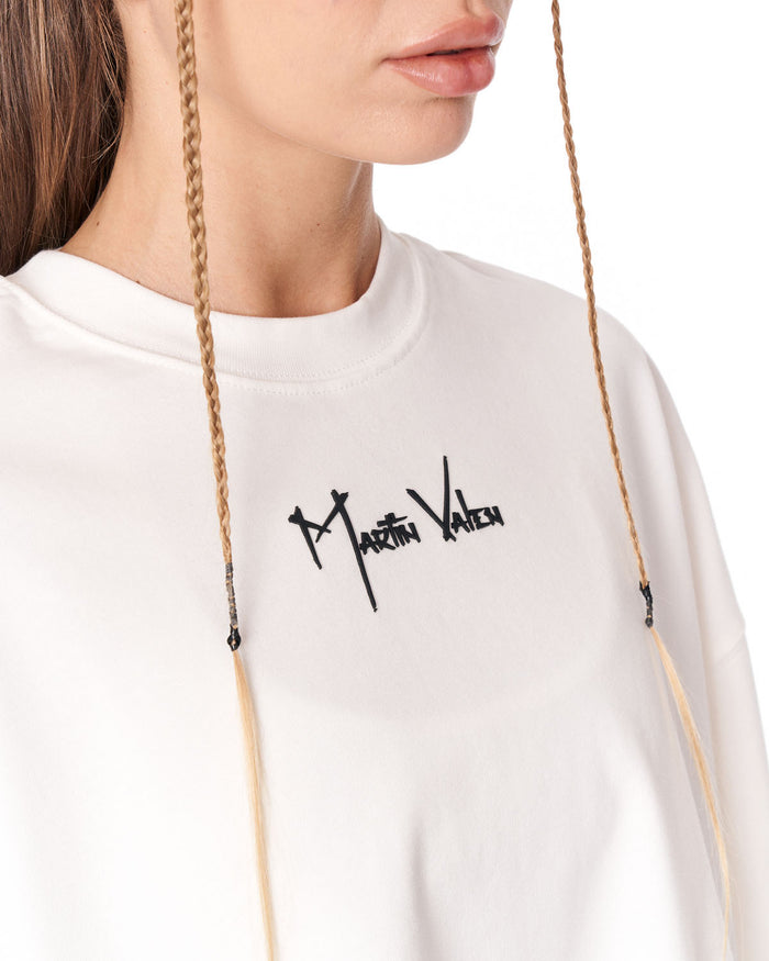 Close-up of a person wearing a white crewneck sweatshirt with a black 'Martin Valet' script logo on the chest. The image shows the lower face, neck, and shoulder, with braided drawstrings hanging down against a plain white background.