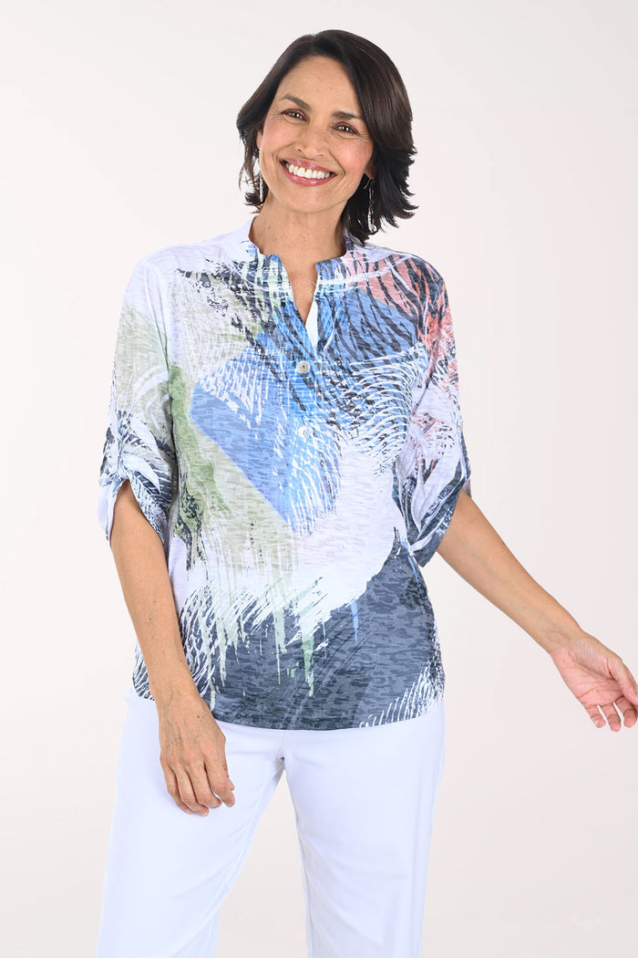Woman wearing a colorful patterned shirt with white pants on a plain background