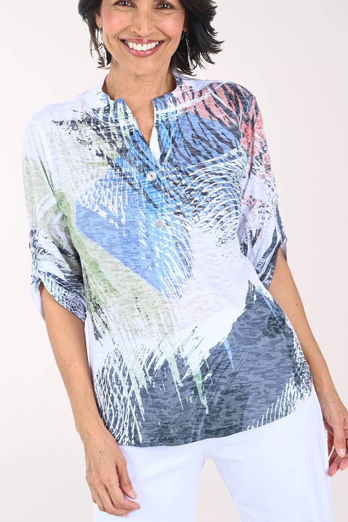 Woman wearing a colorful patterned shirt with white pants on a plain background