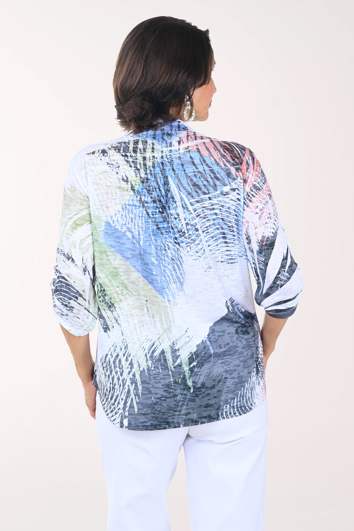 Woman wearing a colorful patterned shirt with white pants on a plain background