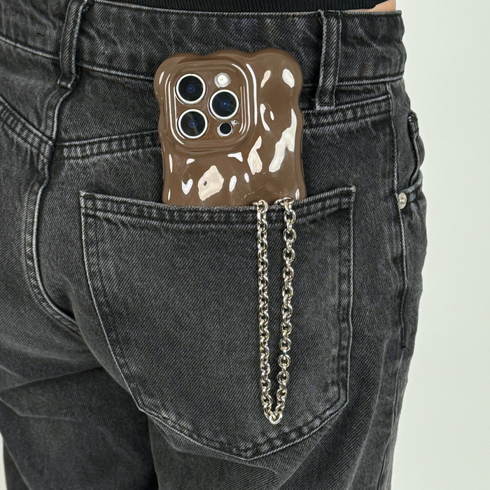 Silver chain phone strap on a brown wavy case, partly visible in the back pocket of black jeans.