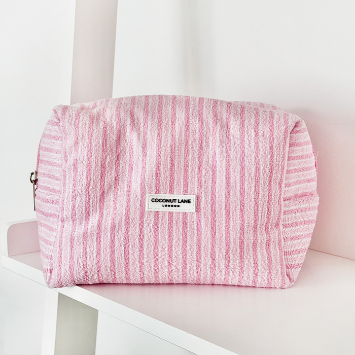 Coconut Lane powder stripes towel makeup bag and matching scrunchie set with pastel striped pattern on a white shelf.