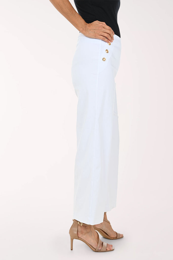 White cropped wide-leg pants with decorative gold-tone buttons on the sides, shown on a model wearing a black top and beige strappy heels against a light studio background.