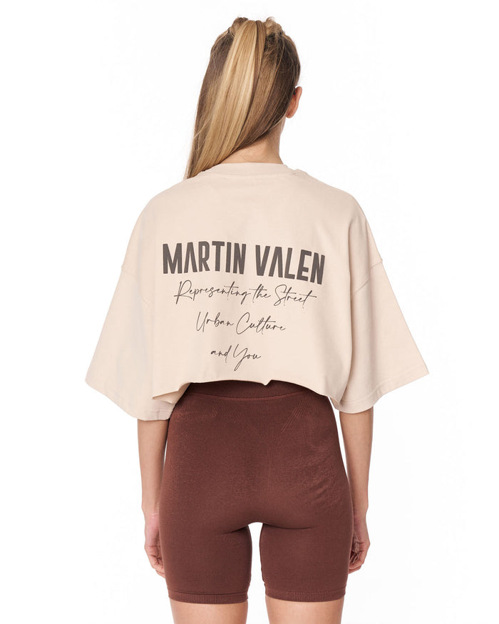 A woman shown from the back wearing a light beige Martin Valen crop top and brown bike shorts against a plain white background.