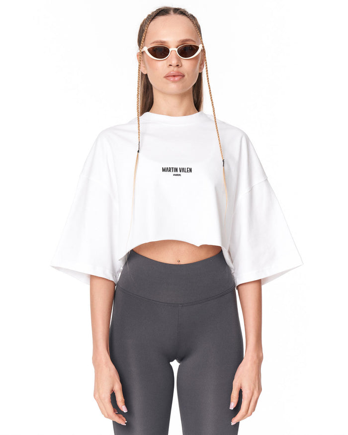 A model wearing a white cropped t-shirt with 'MARTIN VALEN' printed in black on the chest, paired with dark gray leggings, against a plain white background.