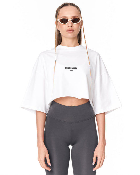 A model wearing a white cropped t-shirt with 'MARTIN VALEN' printed in black on the chest, paired with dark gray leggings, against a plain white background.