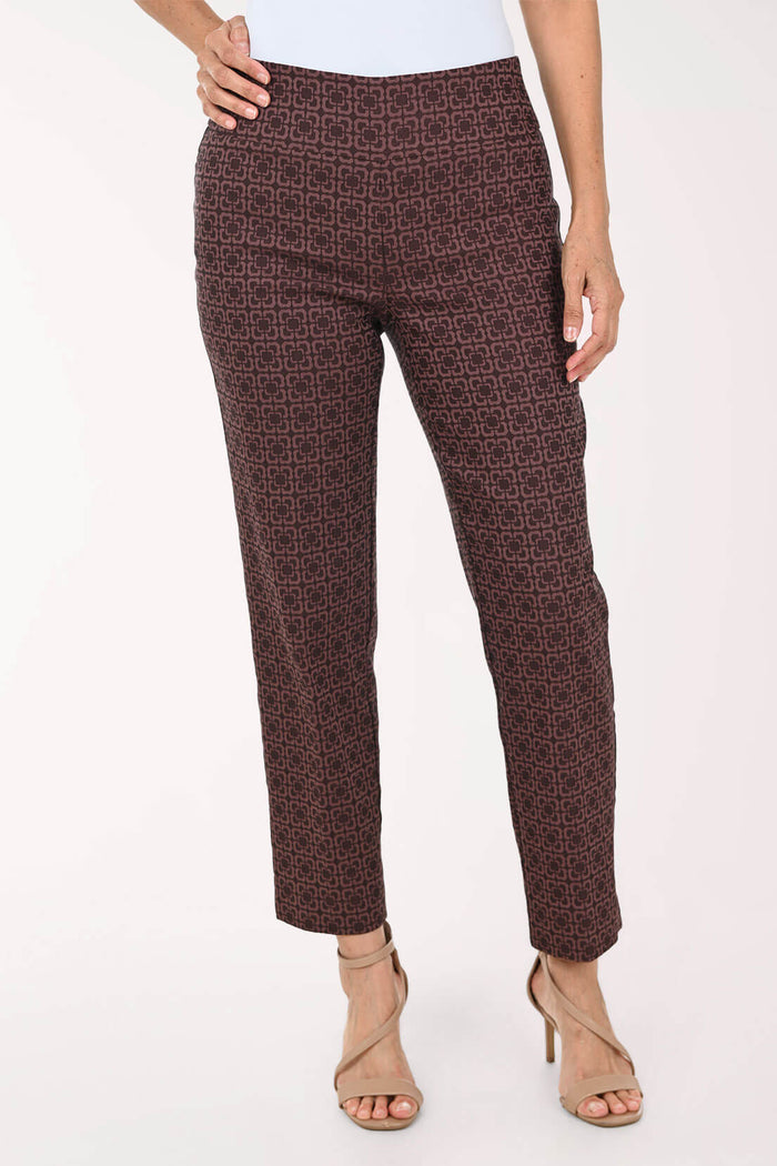 A model wearing a pair of dark brown cropped trousers with a fine geometric pattern, paired with beige high-heeled sandals against a plain white background.