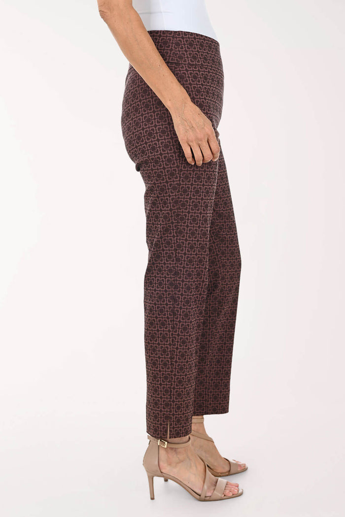A side view of a model wearing dark brown cropped trousers with a subtle geometric pattern, paired with beige high-heeled sandals against a plain white background.