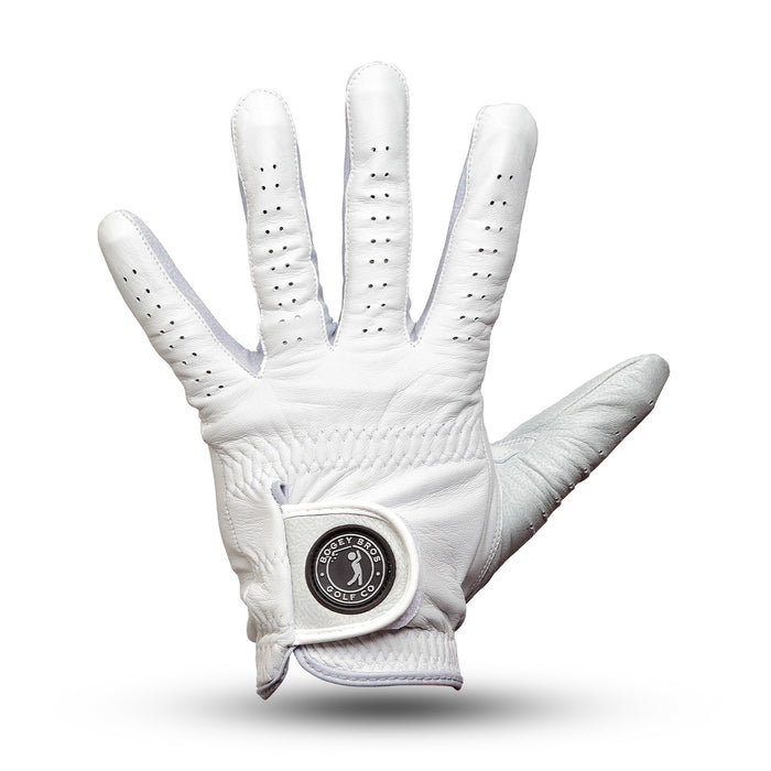 The Stealth Mode - Light - Glove is a white cabretta leather golf glove with small ventilation holes on the fingers and back, an open palm facing forward, and a round black and silver emblem on the Velcro closure for a precise fit.