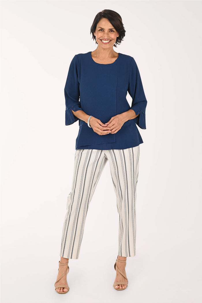A woman modeling a navy blue three-quarter sleeve top paired with off-white pants featuring vertical navy stripes, standing against a plain white studio background.