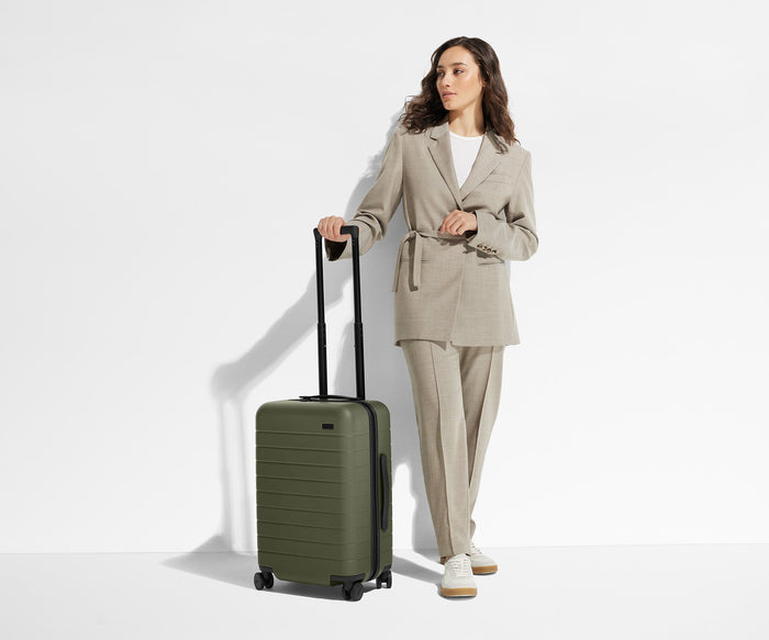 A 5'6" female model is standing next to The Carry-On suitcase and holding onto the raised handle to show size and scale
// 
Model is 5'6"
