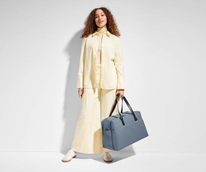 Person carrying the Weekender duffle bag, holding it by the top leather handles
// Model is 5’9”