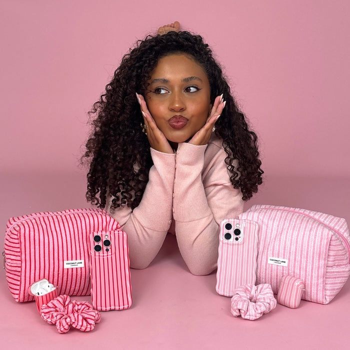Curly-haired woman on a pink background with a Coconut Lane towel scrunchie in cherry stripes in front of her.