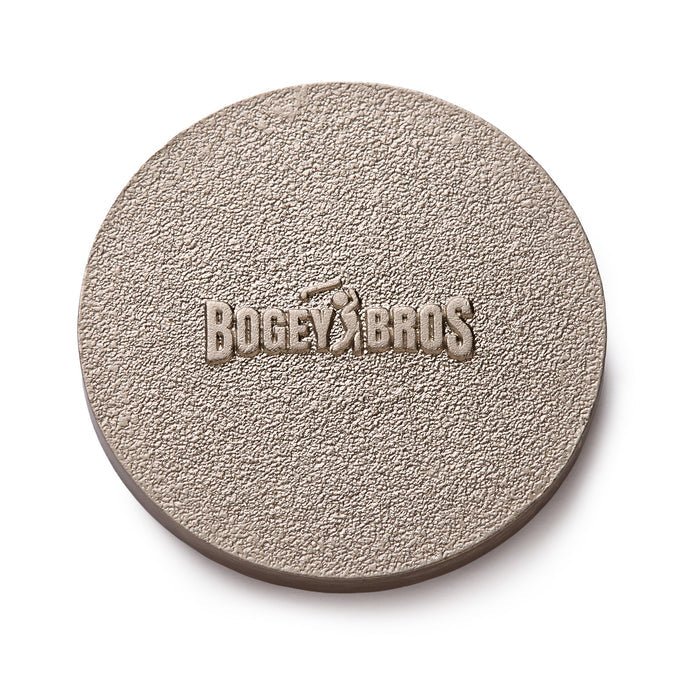 A round, textured, light brown object with the words BOGEY BROS and the silhouette of a golfer embossed in the center. The surface appears rough and grainy.