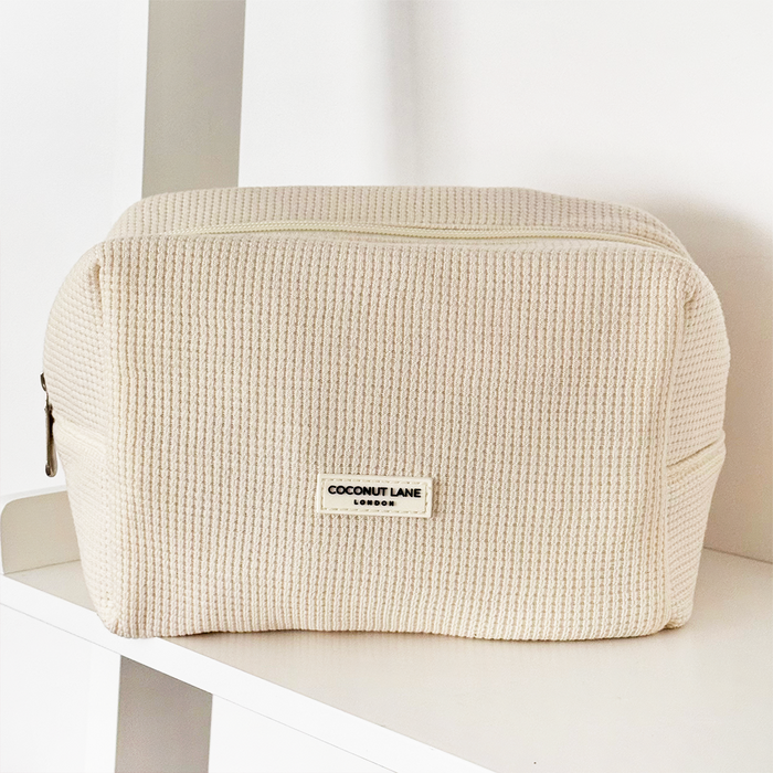 Cream Coconut Lane waffle-textured makeup bag resting on a white shelf.