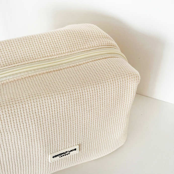 Cream waffle-textured zip makeup bag with subtle Coconut Lane branding, compact and soft for travel.