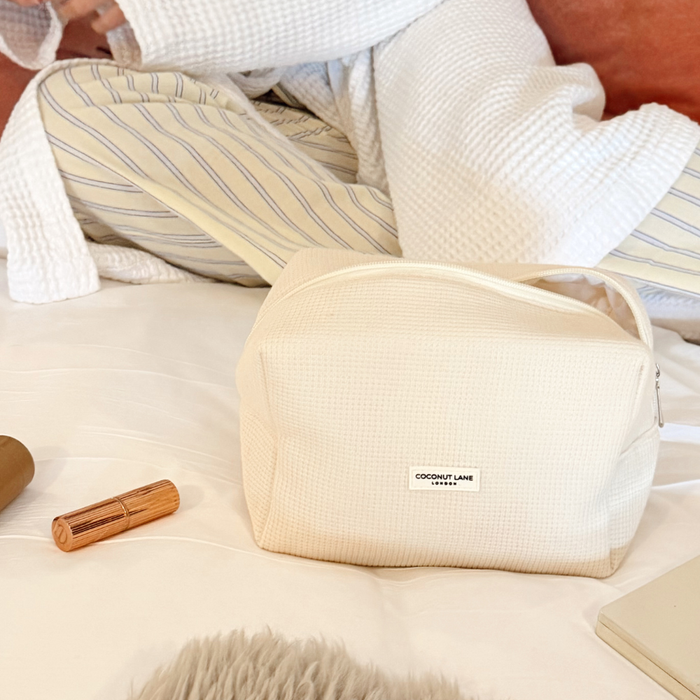 Cream waffle-textured makeup bag on a bed, with a rose gold lipstick placed beside it.